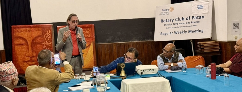 Rtn. Ewerhard Engels speaks into a microphone during his acceptance remarks at the Rotary Club of Patan meeting, 12 October 2026.